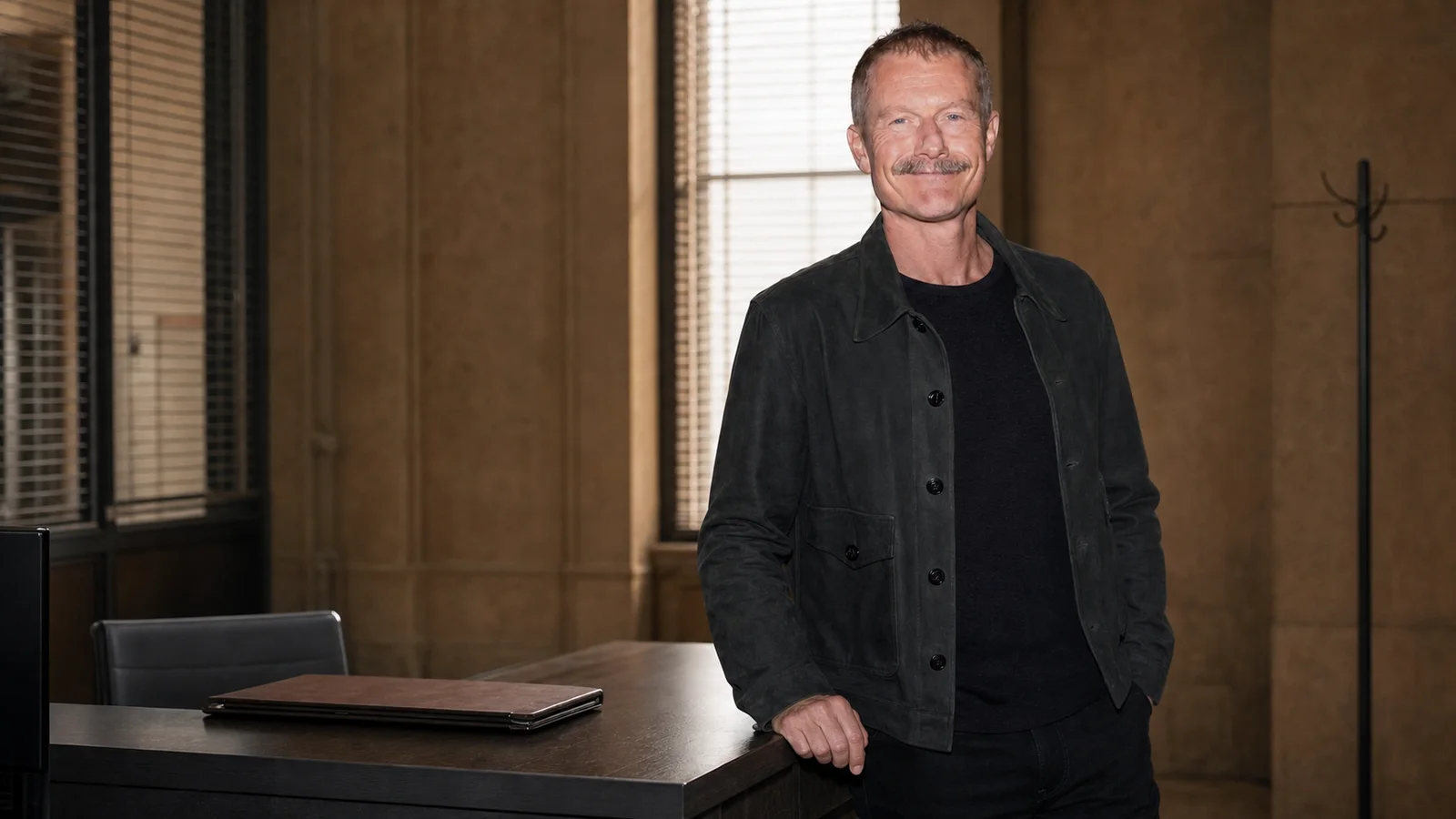 James Badge Dale stands beside an unoccupied precinct desk with a blank folder in a source-grounded editorial portrait.