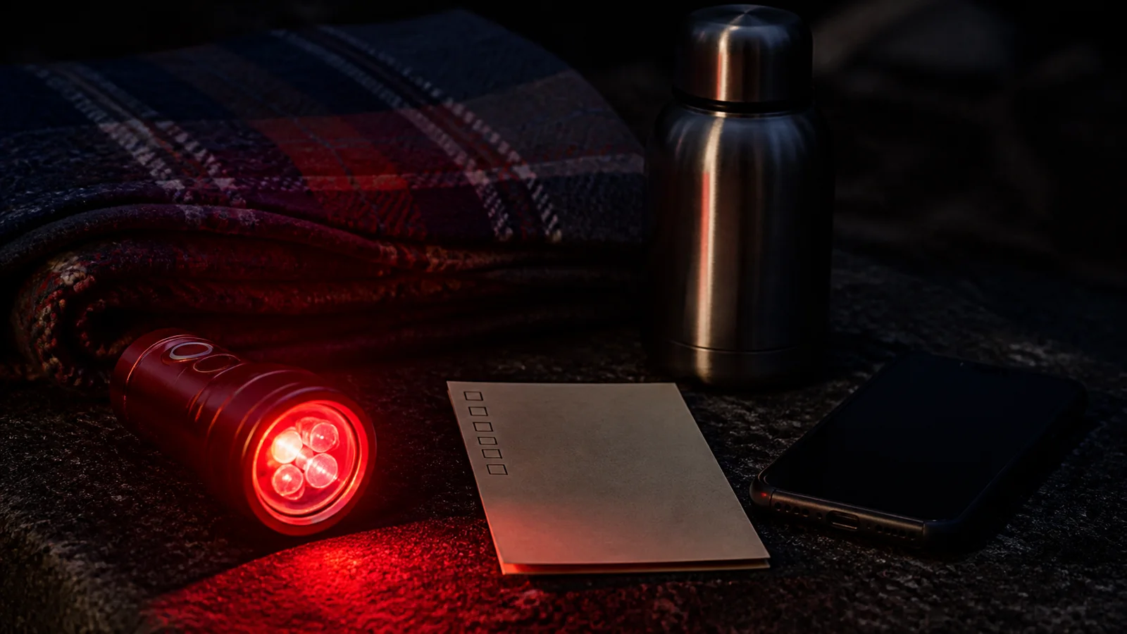 A red flashlight, thermos, blanket, and printed checklist prepared for a meteor shower viewing night