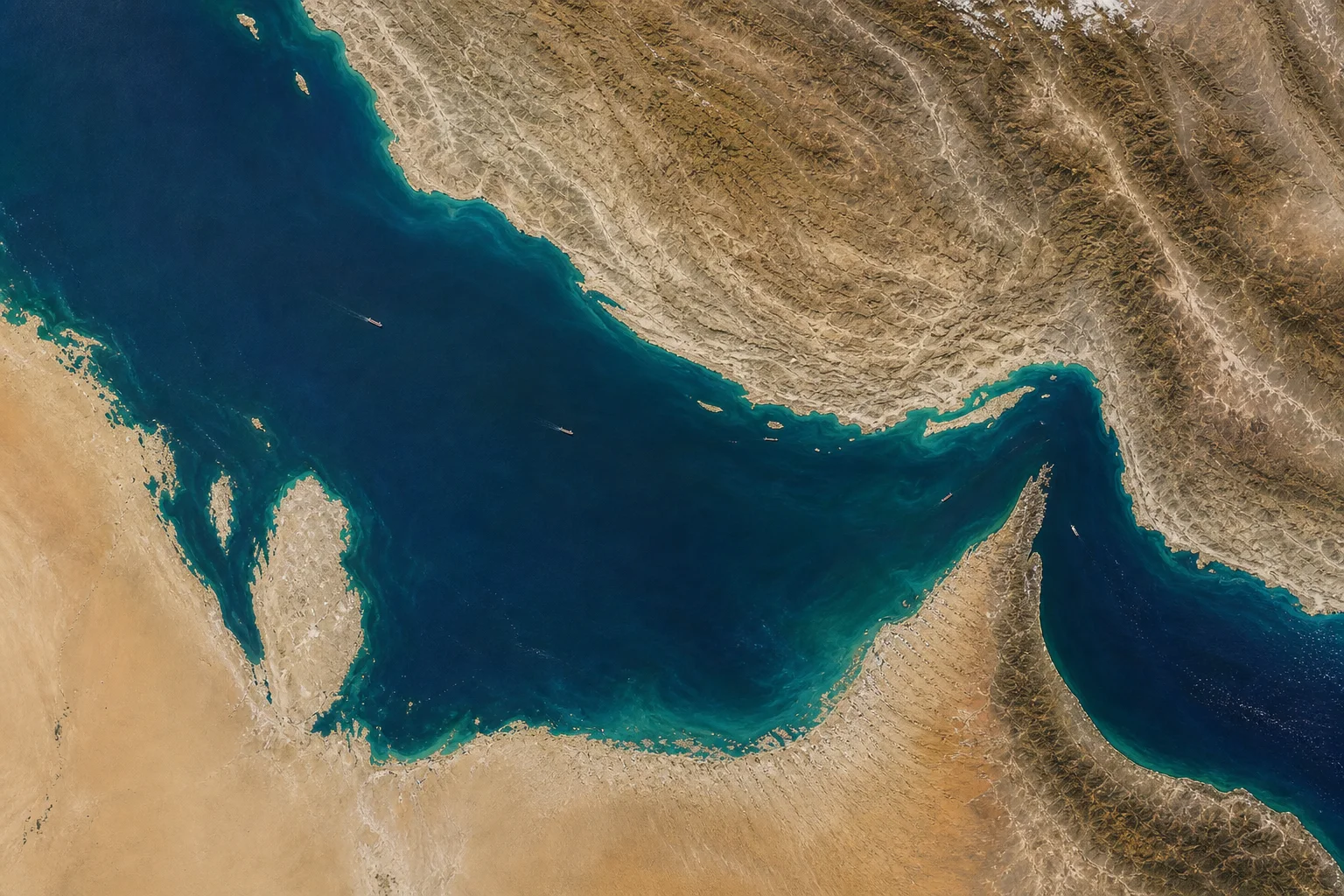 Satellite-based editorial close view of sparse commercial shipping through the Strait of Hormuz.