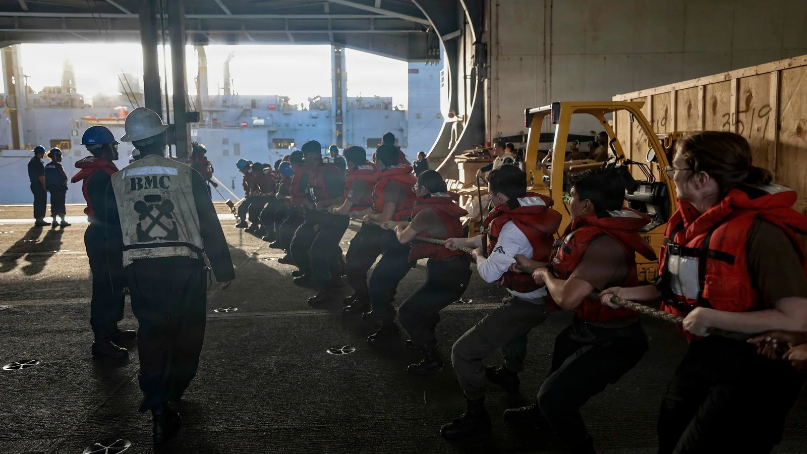 Sailors aboard USS Abraham Lincoln pull a replenishment line together inside the hangar bay.