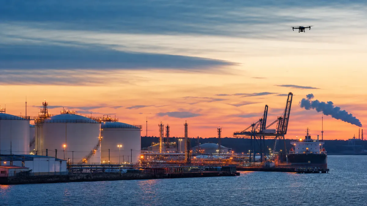 Editorial image of a Baltic oil terminal at dusk with a distant drone silhouette