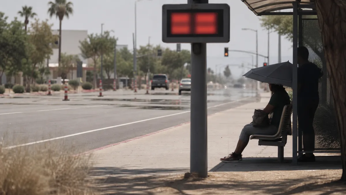 People wait in shade near a sunlit city street during extreme summer heat
