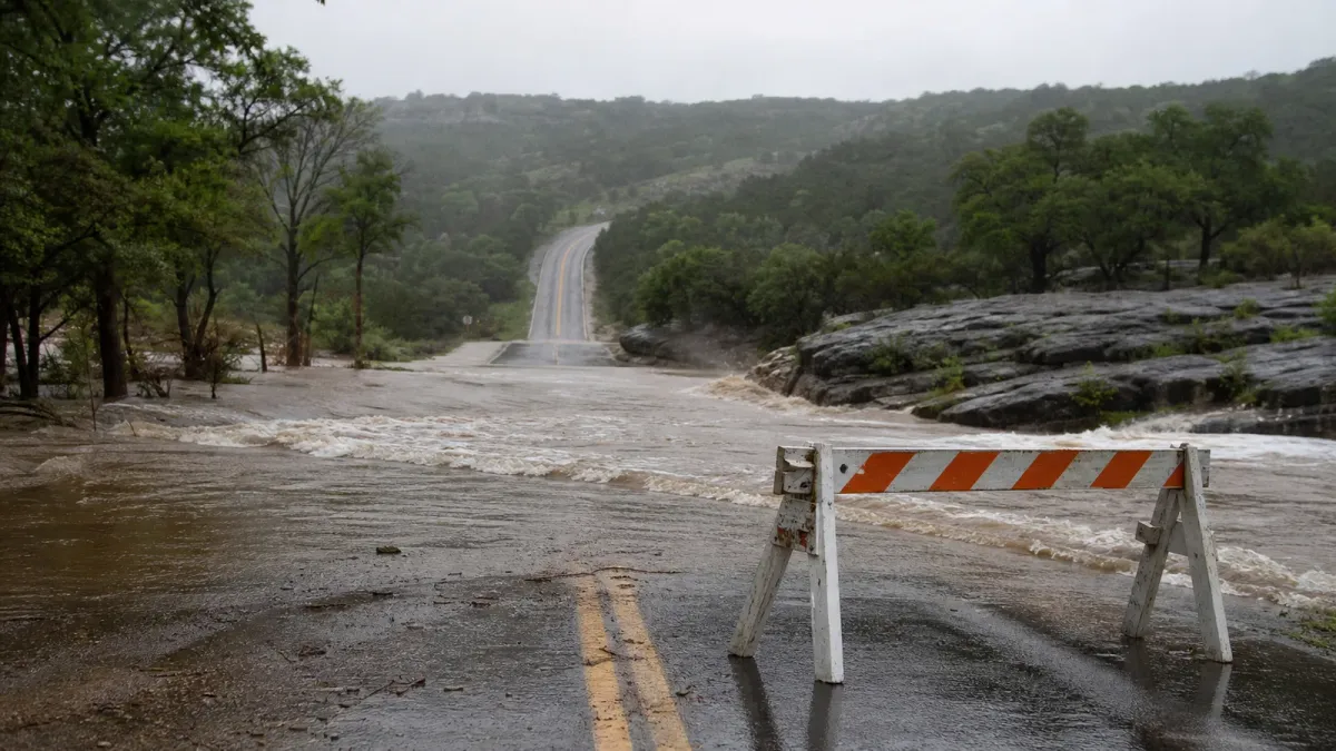 A rain-soaked low-water road crossing in the Texas Hill Country blocked by a barricade as floodwater covers the pavement