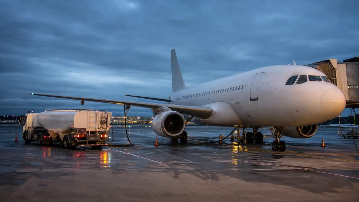 A generic passenger jet being fueled at an airport gate under an overcast evening sky