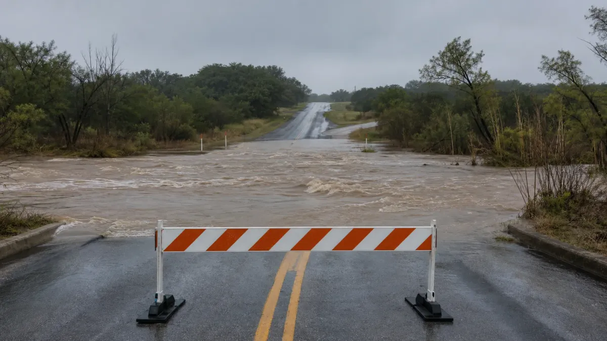Floodwater covers a low-water crossing as a barricade blocks the road in a realistic Texas storm scene
