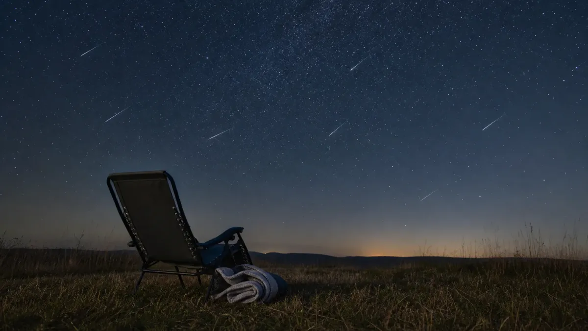 A dark rural viewing spot with a reclining chair beneath subtle meteor streaks in a wide night sky.