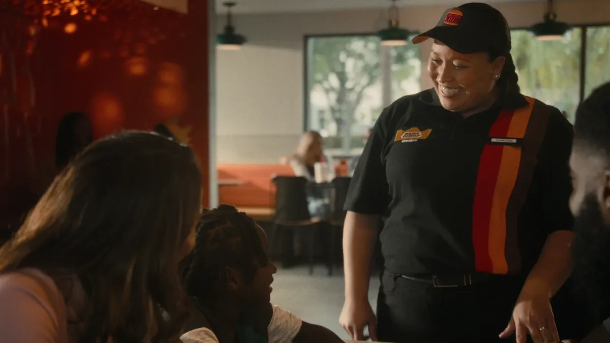 A Burger King team member in uniform speaks with guests inside a restaurant.
