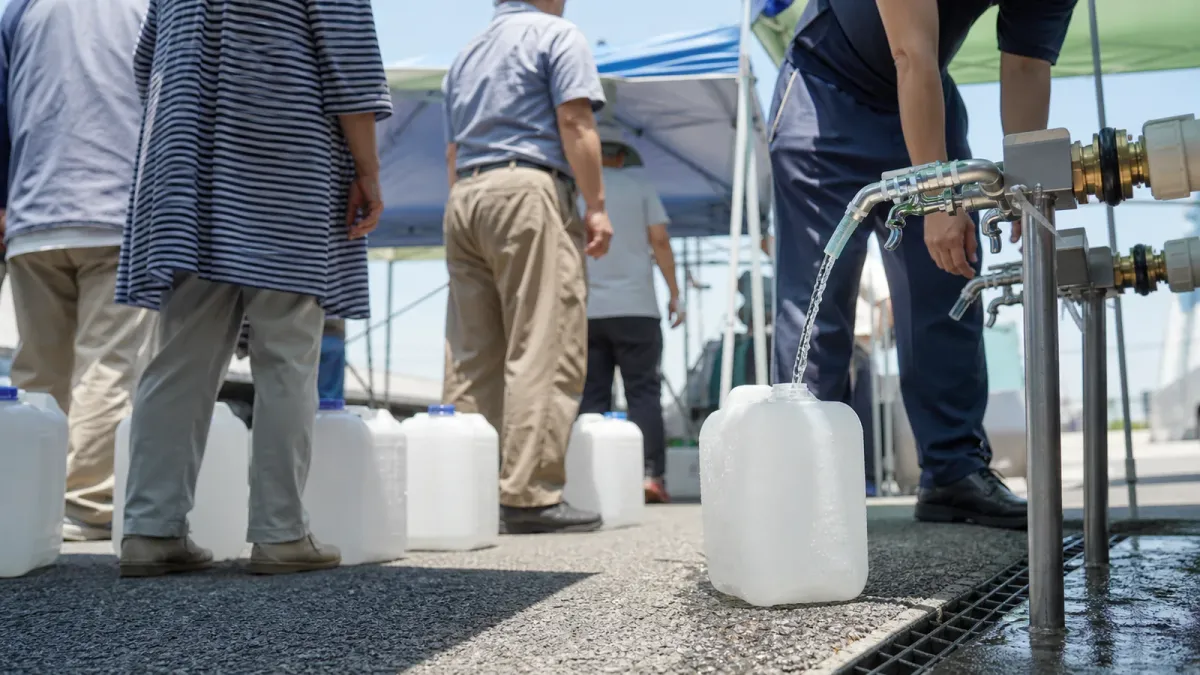 Water containers being filled beneath temporary canopies at a source-grounded earthquake relief point in Hikawa, Kumamoto Prefecture