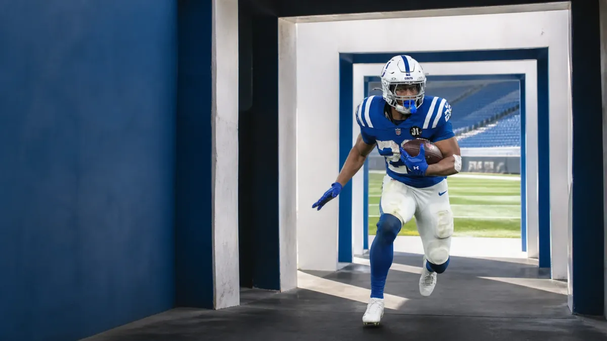 Jonathan Taylor in his Colts number 28 uniform carrying a football through a sequence of stadium tunnel arches toward the field