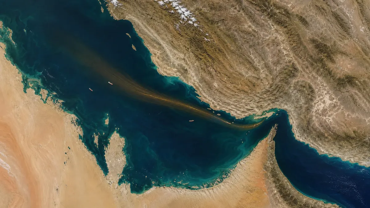 Satellite-based editorial view of the Strait of Hormuz with a trade corridor narrowing through the channel.