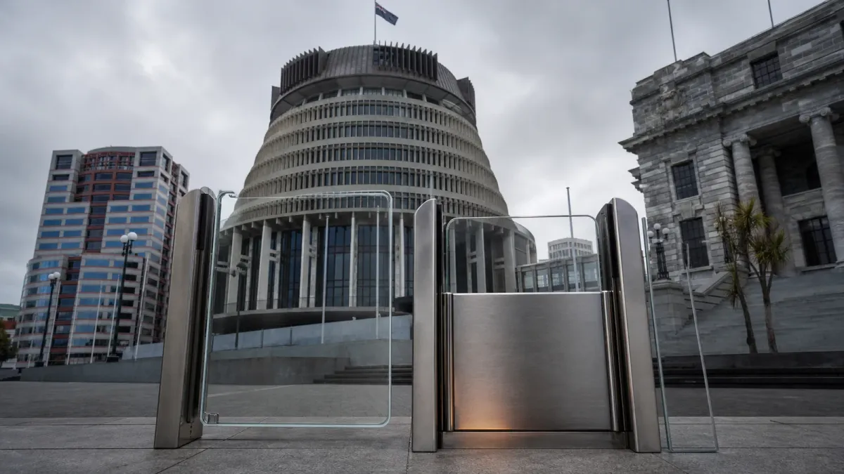 New Zealand Parliament’s Beehive behind a staged split glass-and-steel access threshold holding a neutral phone-shaped panel