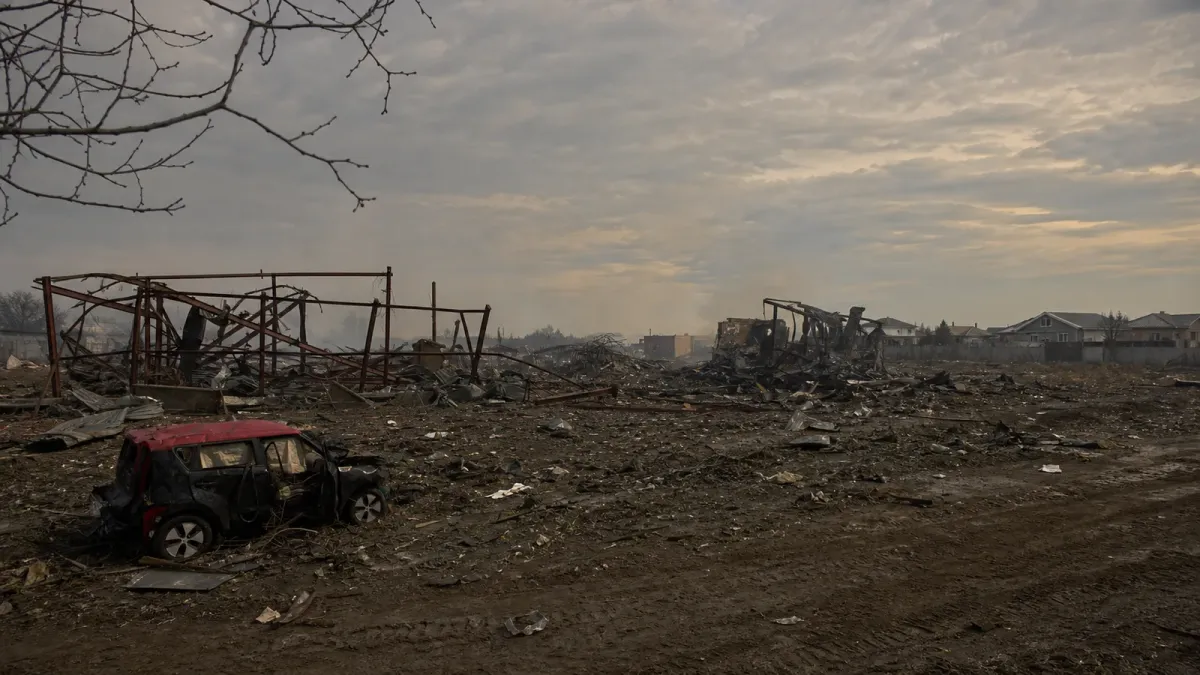 Collapsed steel warehouse frames and a damaged vehicle in the smoke-muted aftermath of the Myla strike