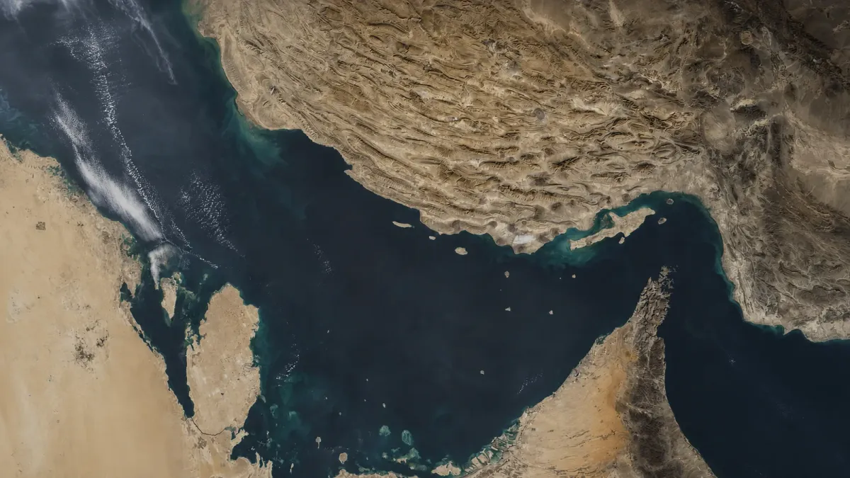 Satellite view of the Strait of Hormuz between Iran and Oman under a restrained editorial shadow
