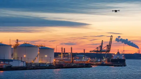 Editorial image of a Baltic oil terminal at dusk with a distant drone silhouette