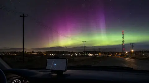 Aurora above a small town with power lines, a communications tower and a generic navigation screen