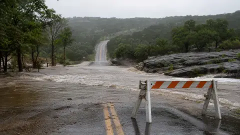 A rain-soaked low-water road crossing in the Texas Hill Country blocked by a barricade as floodwater covers the pavement