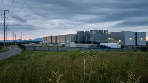 A generic large data center near utility lines under an overcast evening sky