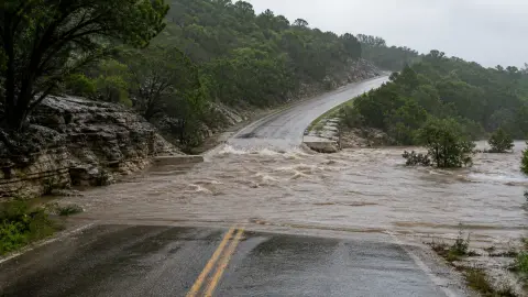 Muddy floodwater covering a low road while a dry route rises uphill in a generic Hill Country scene
