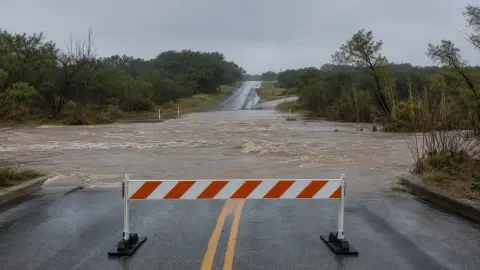 Floodwater covers a low-water crossing as a barricade blocks the road in a realistic Texas storm scene