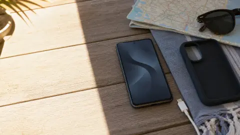 A smartphone cooling in the shade beside a loose case, unplugged cable and folded map
