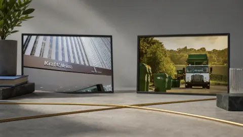 A tabletop editorial set shows framed Kraft Heinz headquarters and WM truck photos behind two crossing gold rails