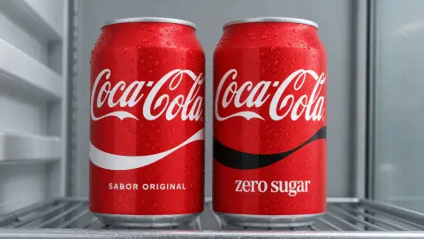 Updated Coca-Cola Original Taste and Zero Sugar cans side by side, distinguished by white and black ribbon designs