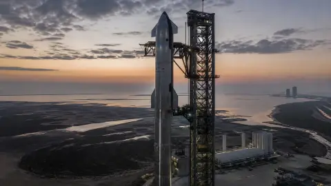 SpaceX Starship and Super Heavy on the Starbase pad under a dim sky, framed as a grounded test vehicle awaiting another launch attempt