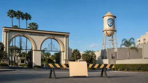 Paramount Skydance and Warner Bros. Discovery studio landmarks separated by a temporary legal pause barrier.