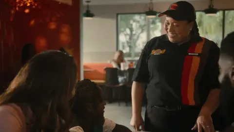 A Burger King team member in uniform speaks with guests inside a restaurant.