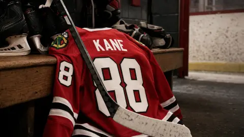 A red Blackhawks number 88 Kane jersey and hockey stick staged in a locker-room return scene