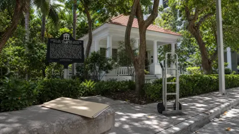 Historic Jackson Cottage and Dade Heritage Trust setting in Brickell framed with a civic folder and moving dolly to suggest the approved sale and possible relocation.