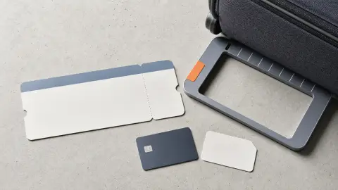 A travel-booking still life with a blank ticket, carry-on bag, measuring frame and payment card arranged as a fare check.