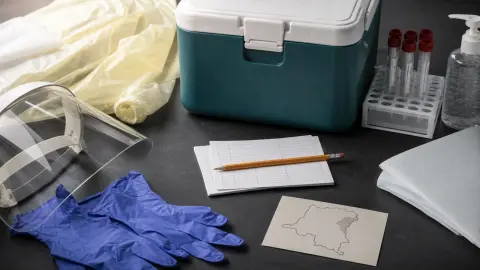 Protective gloves, a face shield, tracing cards and a lab cooler arranged as an interrupted Ebola response kit.