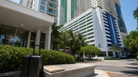 The Club at Brickell Bay at 1200 Brickell Bay Drive with a small suitcase and closed folder near a condo entrance, suggesting a short-term-rental access dispute.
