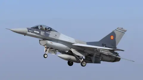 A Romanian Air Force F-16 in flight with its roundel and tail markings visible against a blue sky