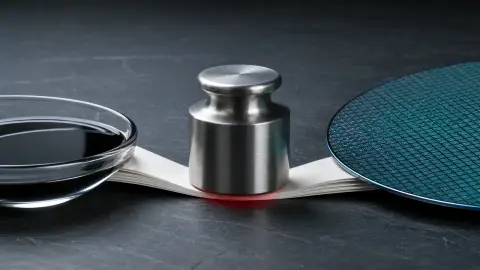 Crude oil, a steel rate weight and a silicon wafer press inward on blank financial papers in a tense tabletop still life.