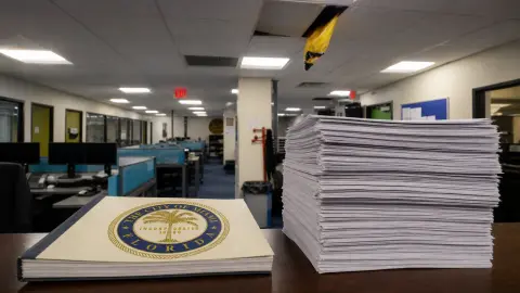 City of Miami financing papers sit inside a source-grounded police workspace beneath a damaged ceiling, with a larger stack suggesting the bond’s added repayment costs.