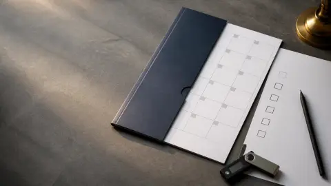 A blank legislative folder, calendar page, checklist, pen, and hardware wallet arranged on a desk