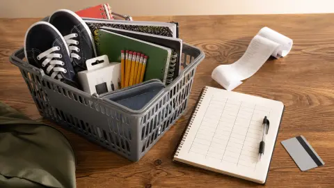 Back-to-school supplies, a budget sheet, a receipt and a payment card arranged beside a shopping basket