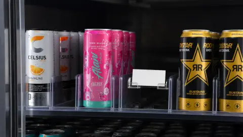 Recognizable Celsius, Alani Nu and Rockstar Energy cans compressed on a retail cooler shelf with a blank investor note nearby.