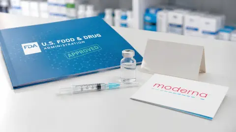 FDA and Moderna references beside a generic vaccine vial and syringe on a pharmacy counter.