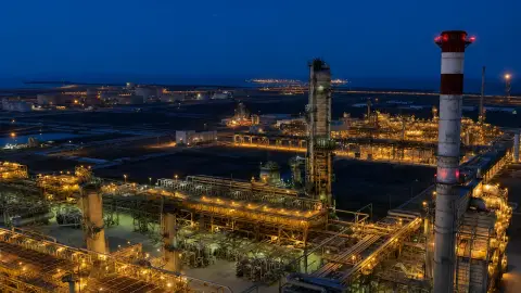 Aramco refinery towers and pipelines lit at dusk near the Red Sea