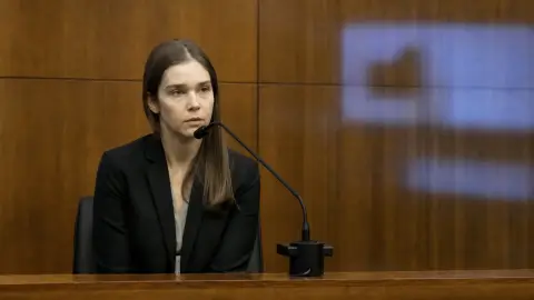 Source-grounded editorial image of psychiatrist Jennifer Tufts at the witness stand with warm courtroom wood and a restrained cool light cue for telehealth.