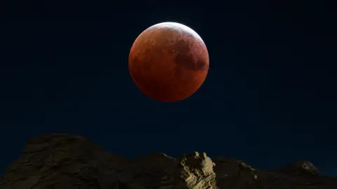 Deep partial lunar eclipse with a thin bright rim above a dark horizon