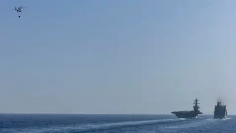 USS Abraham Lincoln sails beside a replenishment oiler as a helicopter carries cargo overhead.