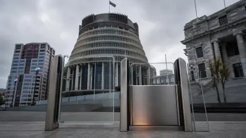 New Zealand Parliament’s Beehive behind a staged split glass-and-steel access threshold holding a neutral phone-shaped panel