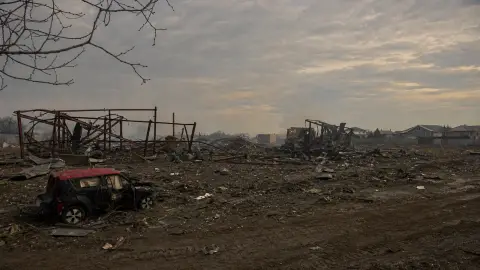 Collapsed steel warehouse frames and a damaged vehicle in the smoke-muted aftermath of the Myla strike