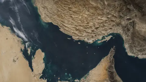 Satellite view of the Strait of Hormuz between Iran and Oman under a restrained editorial shadow