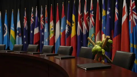 Pacific Islands Forum flags behind a summit table with one empty place offset from aligned blank folders