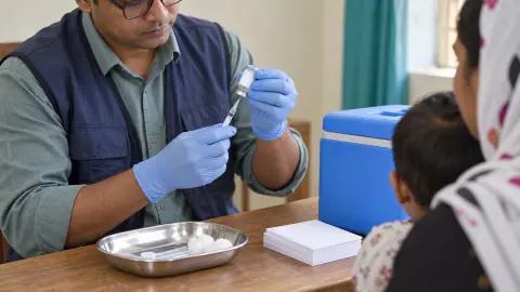 A source-grounded editorial view of measles vaccine preparation at a child vaccination clinic in Bangladesh